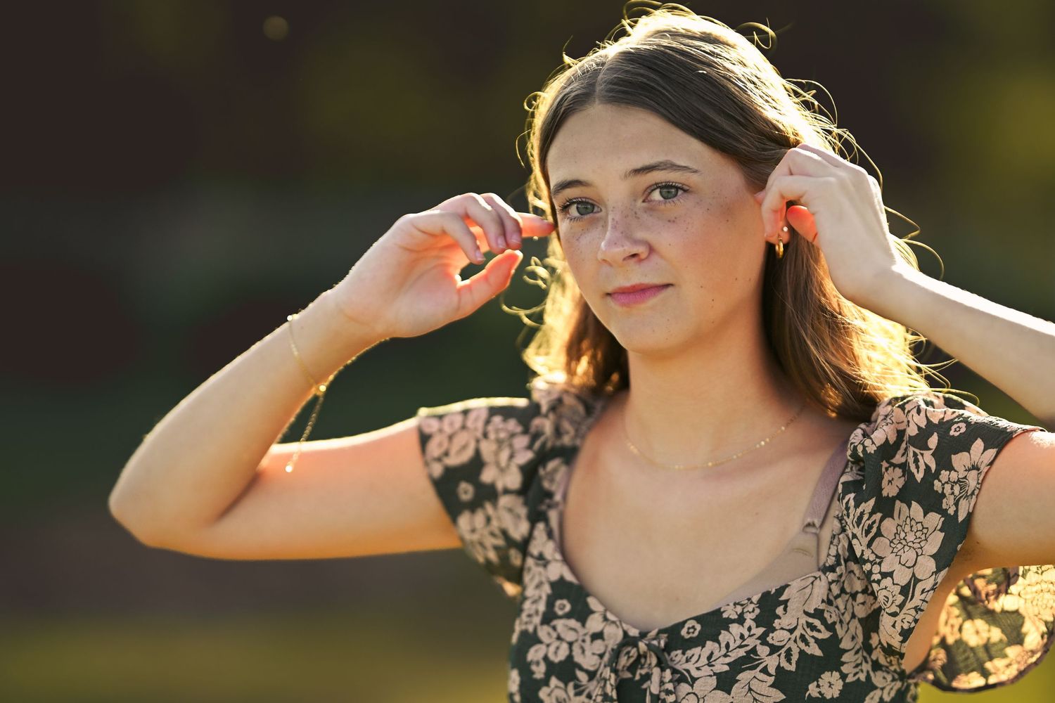Person in floral dress poses outdoors in golden sunlight during sunset photo session.
