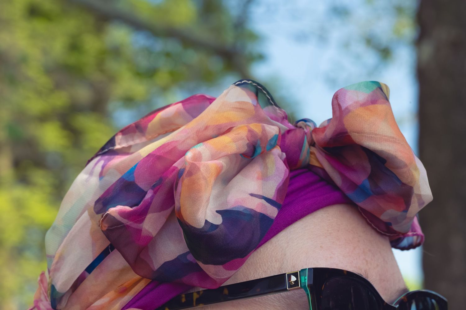 Woman wearing a colorful multicolored silk scarf wrapped around her head outdoors.