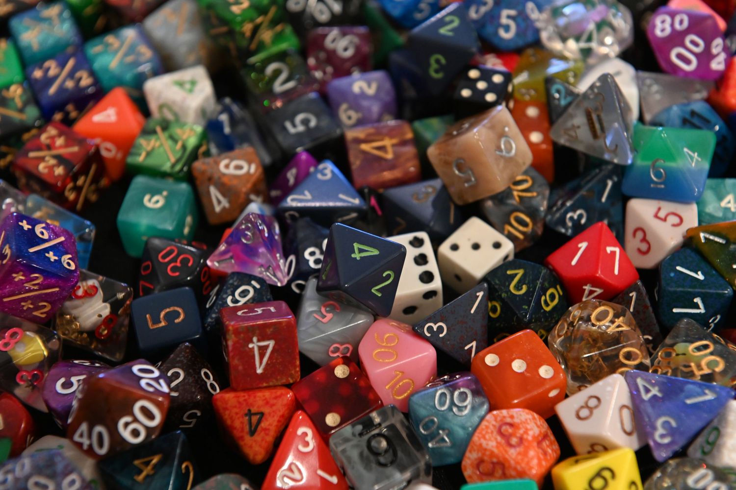 A colorful collection of polyhedral gaming dice featuring various shapes and numbers in red, purple, green, and other colors.