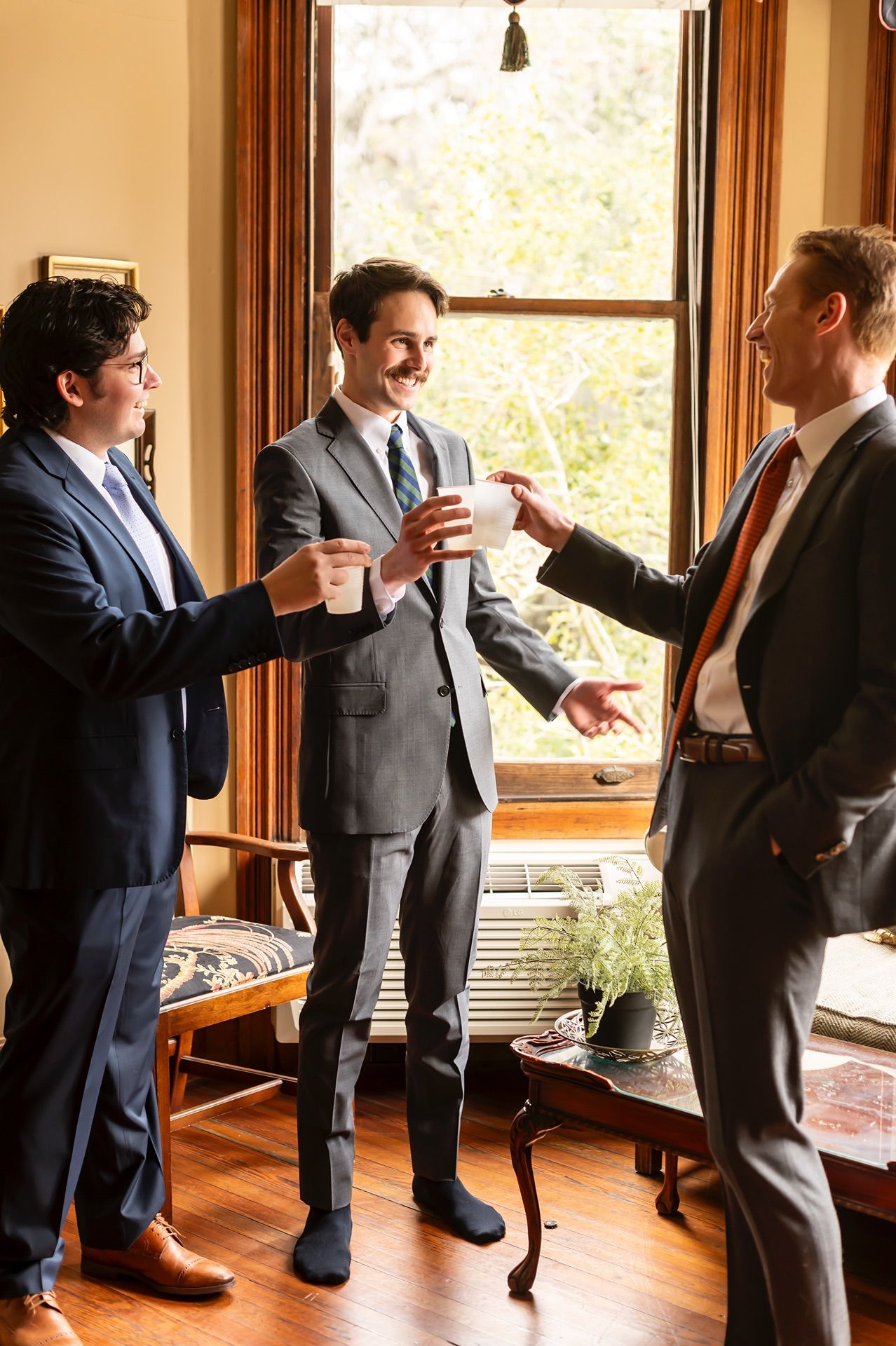 Sequence of people in suits celebrating and dancing in a room with wooden floors and bright windows.
