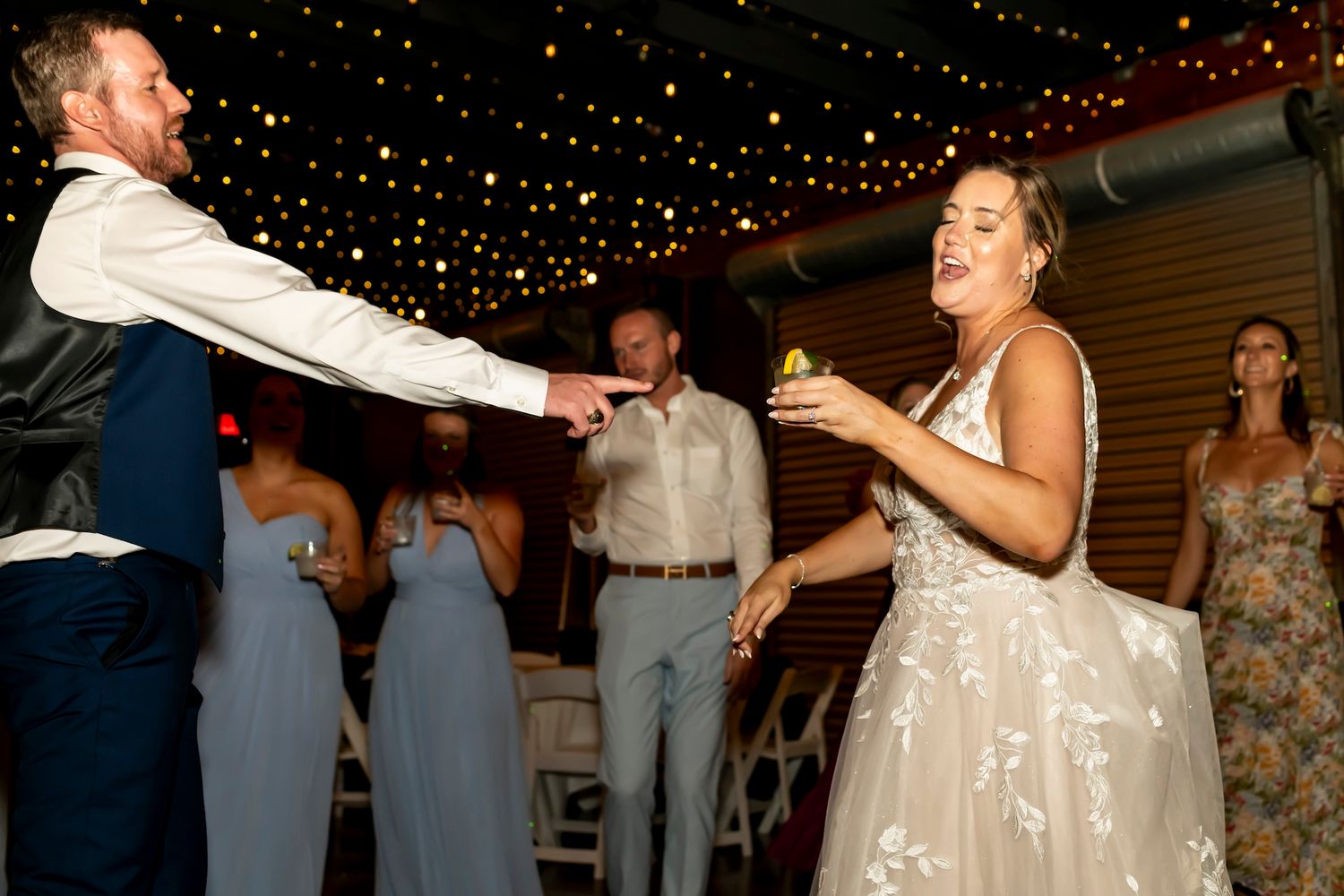 A couple dances together during what appears to be their first dance at a wedding reception with sparkling lights overhead.