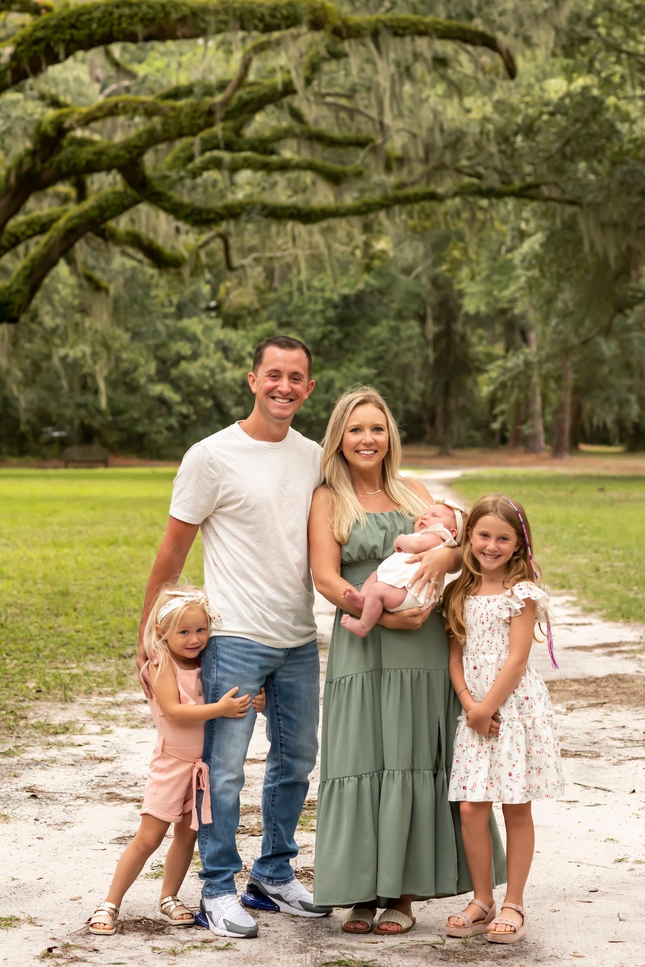 Family photo session under moss-draped oak trees on a sandy path in a natural outdoor setting.