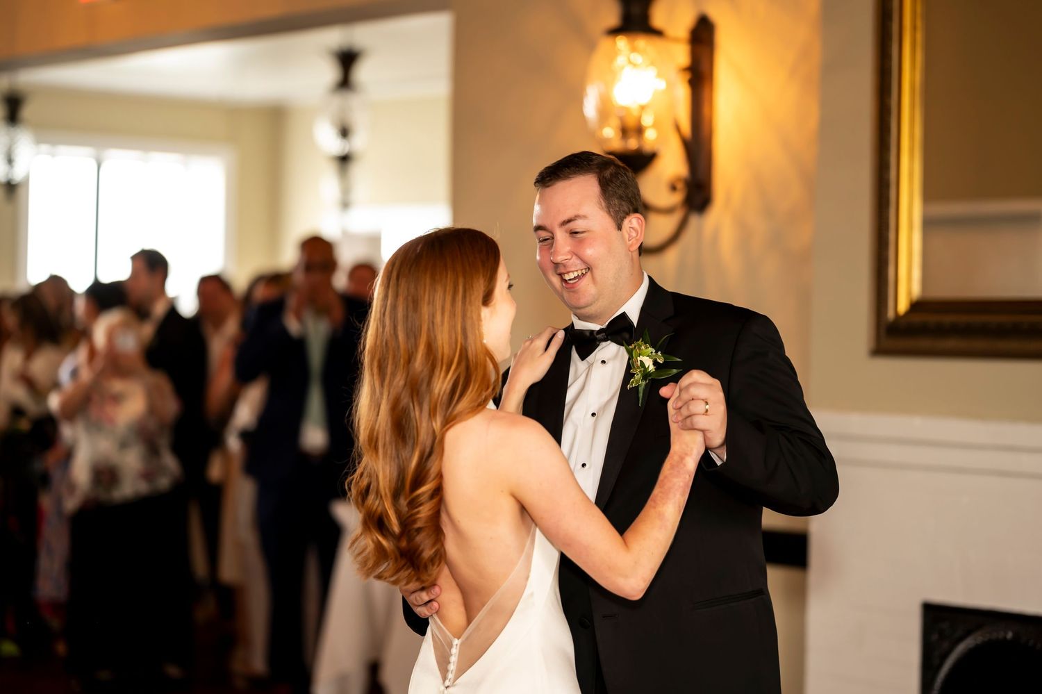 A bride and groom share their first dance at an elegant ballroom reception with guests watching in the background.