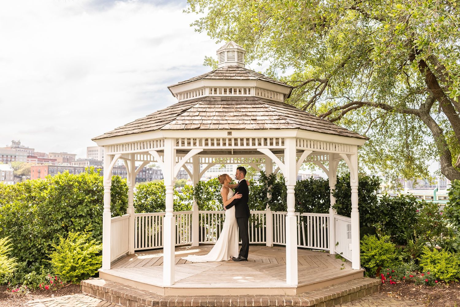 A classic white gazebo in a garden setting surrounded by lush greenery and trees.