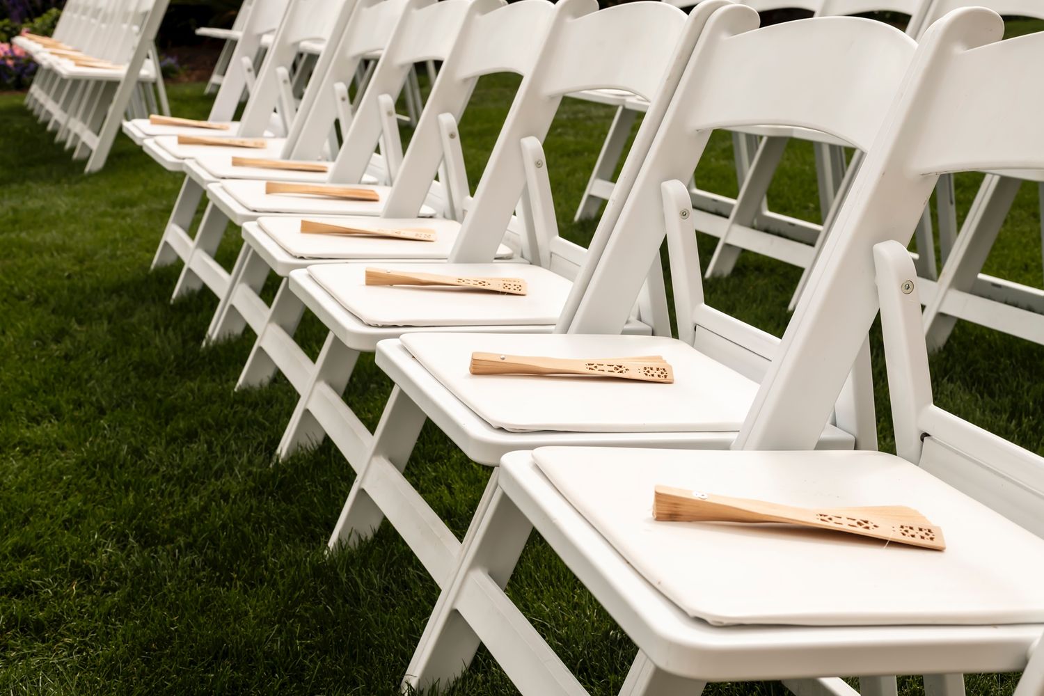 Row of white folding chairs set up on grass lawn for outdoor wedding ceremony.
