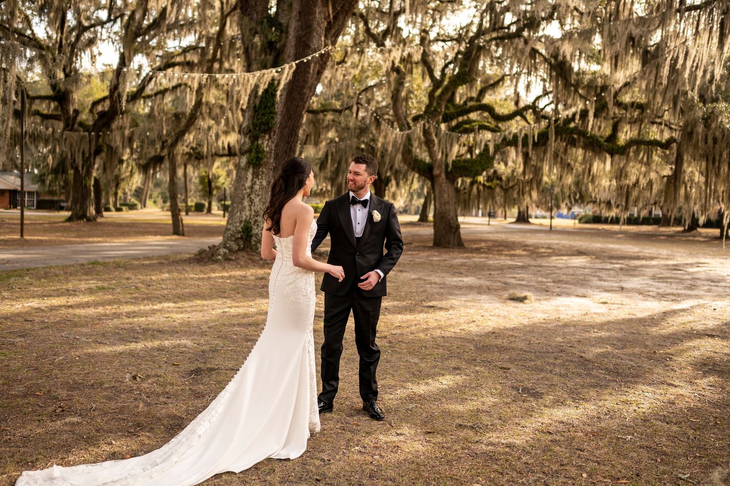 A couple shares a joyful moment under Spanish moss-draped oak trees during their outdoor wedding ceremony.