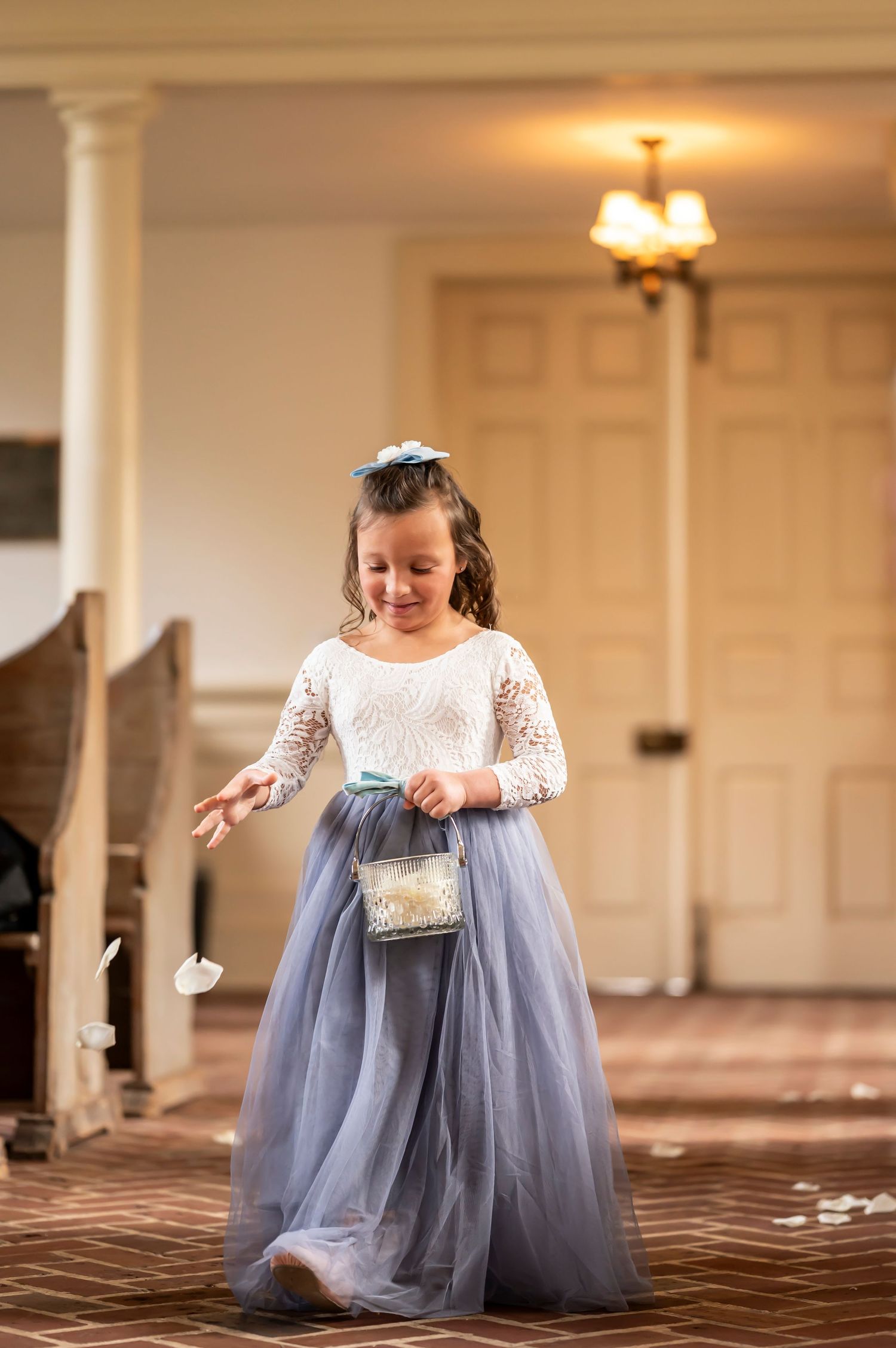A girl in a white lace dress and blue tulle skirt sits and dances in an elegant ballroom.