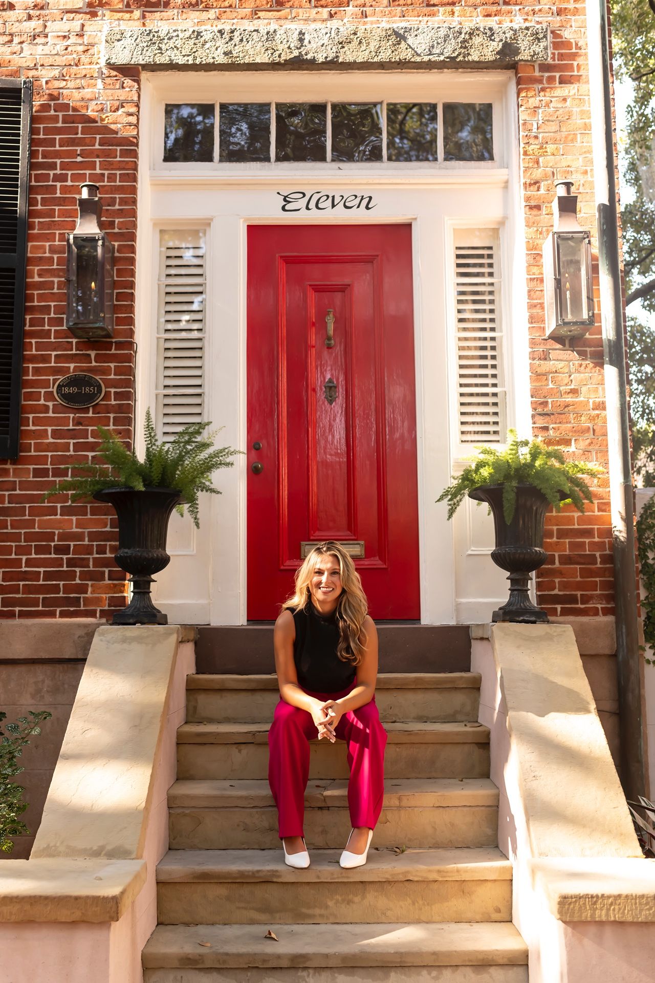A red door numbered 'Eleven' adorns a brick townhouse with white trim and decorative potted plants on the entry steps.