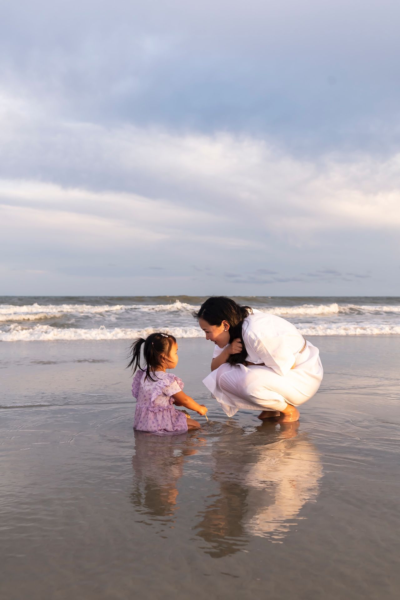 Two people lying in shallow ocean water at the beach during sunset playing in the waves.