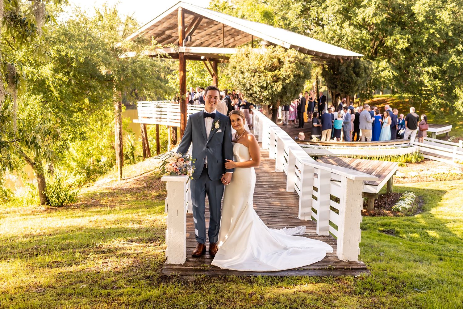 A romantic wedding scene with a couple embracing under a rustic wooden pavilion in a sunny garden setting.