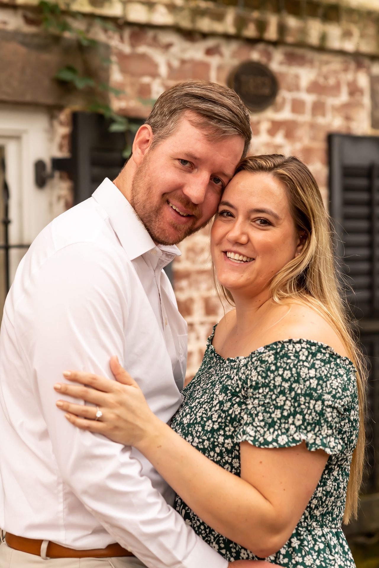 A couple shares a tender moment while embracing against a rustic brick wall background.
