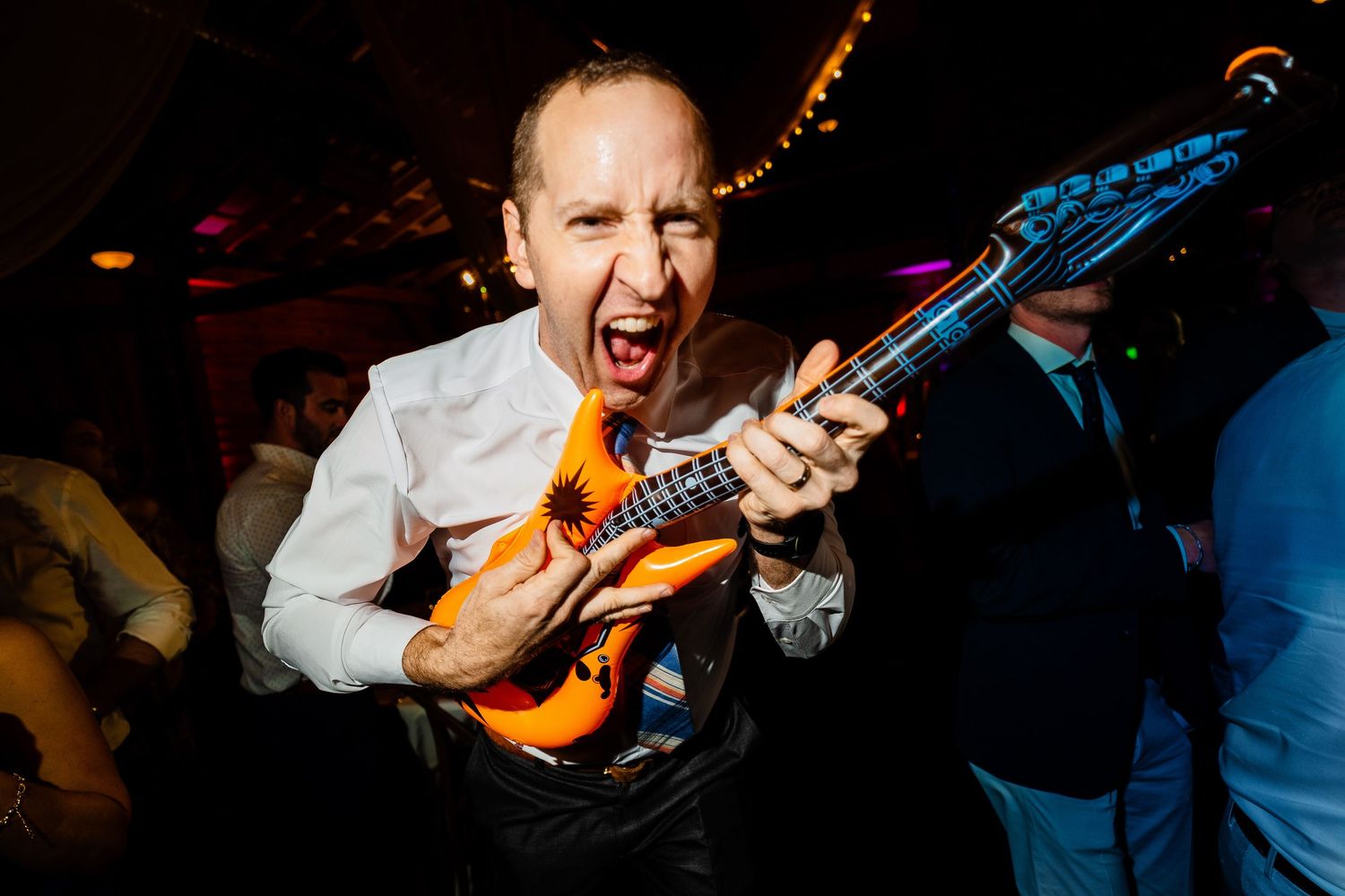 A guitarist performs passionately on stage at a dimly lit concert venue with colorful lighting effects in the background.