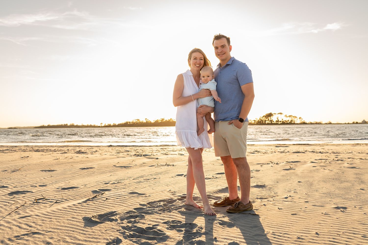 Family of three enjoying a sunset moment together on a sandy beach during golden hour.