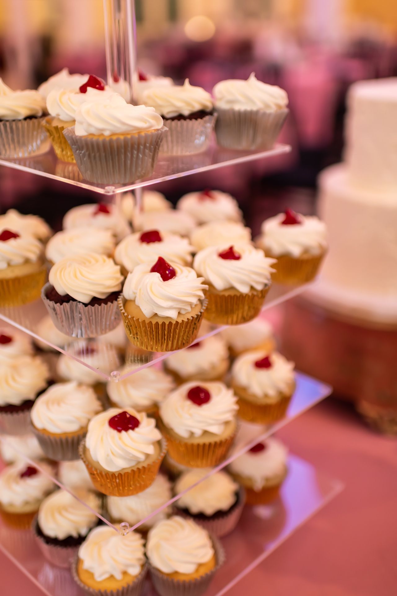 White frosted cupcakes topped with red berries displayed on a tiered stand at an elegant event.