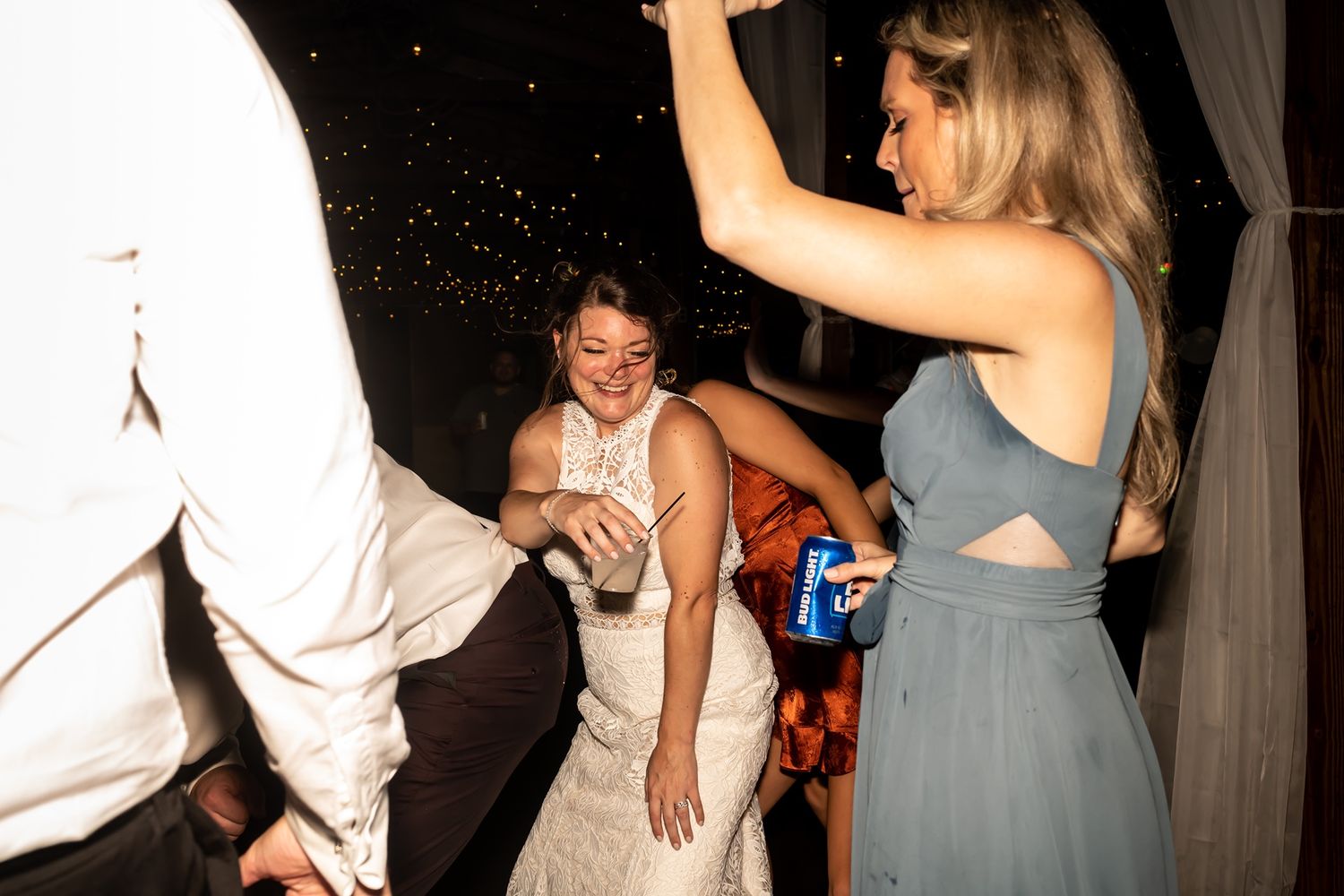 A group dances together on a dark dance floor during what appears to be a wedding reception celebration.