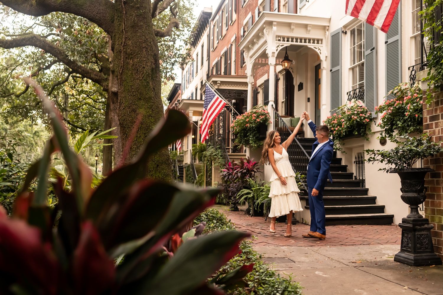A historic townhouse entrance decorated with American flags and flowering plants along the steps in Savannah, Georgia.