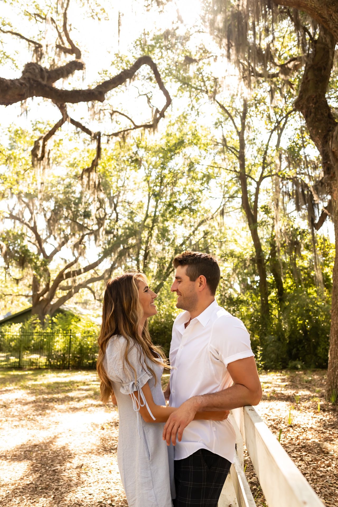 A couple embraces under Spanish moss-draped oak trees in a sun-dappled natural setting.