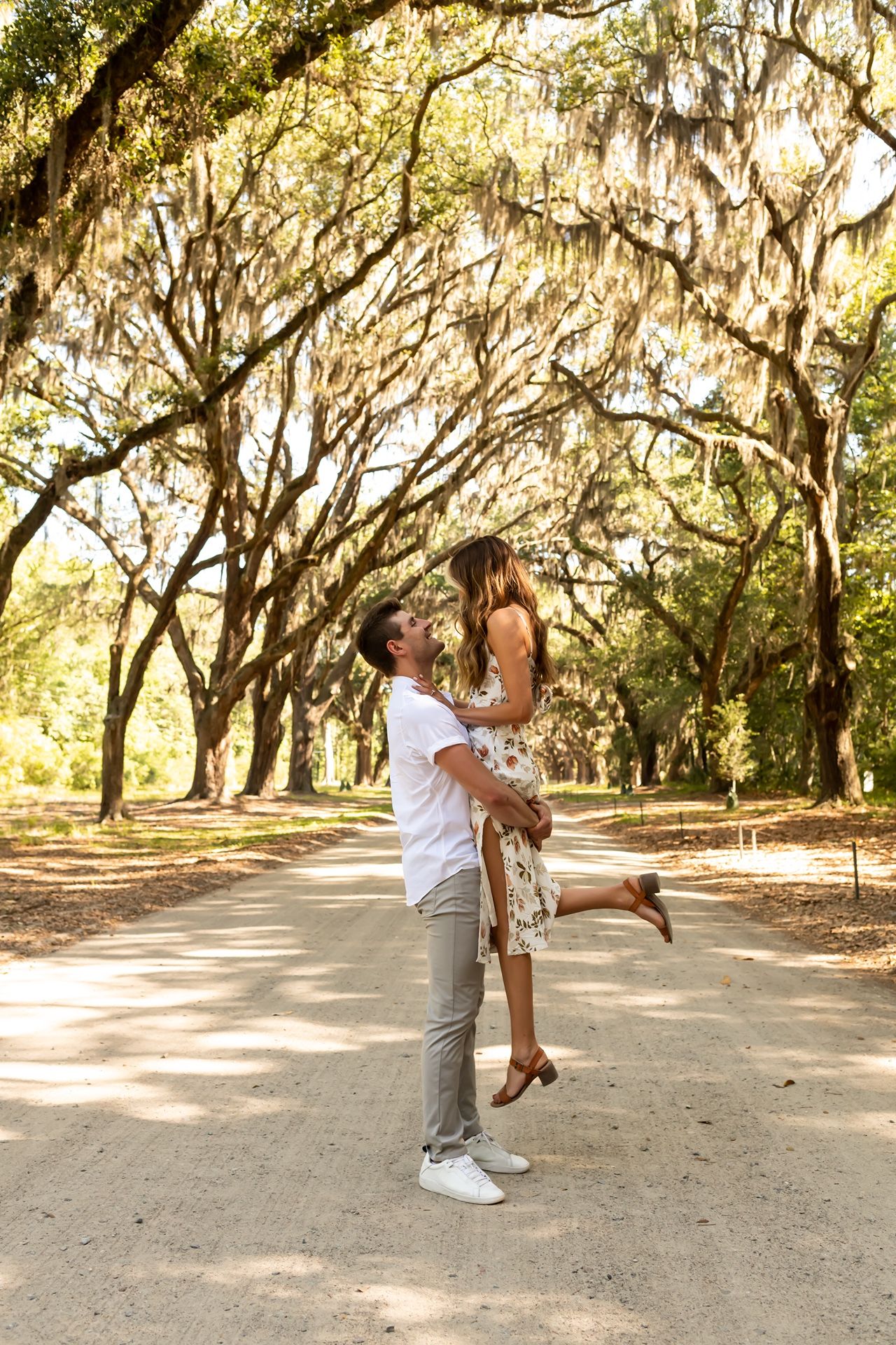 A romantic couple dancing together under a canopy of moss-draped oak trees in a park setting.