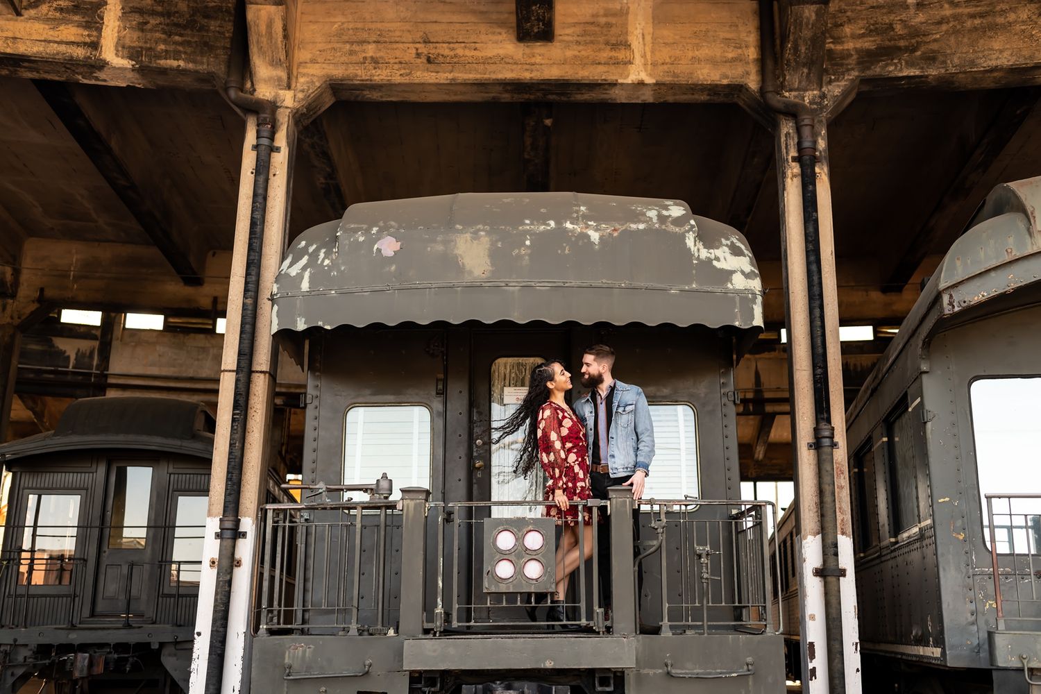 A vintage train car interior features ornate wooden railings and architectural details in an antique railway setting.