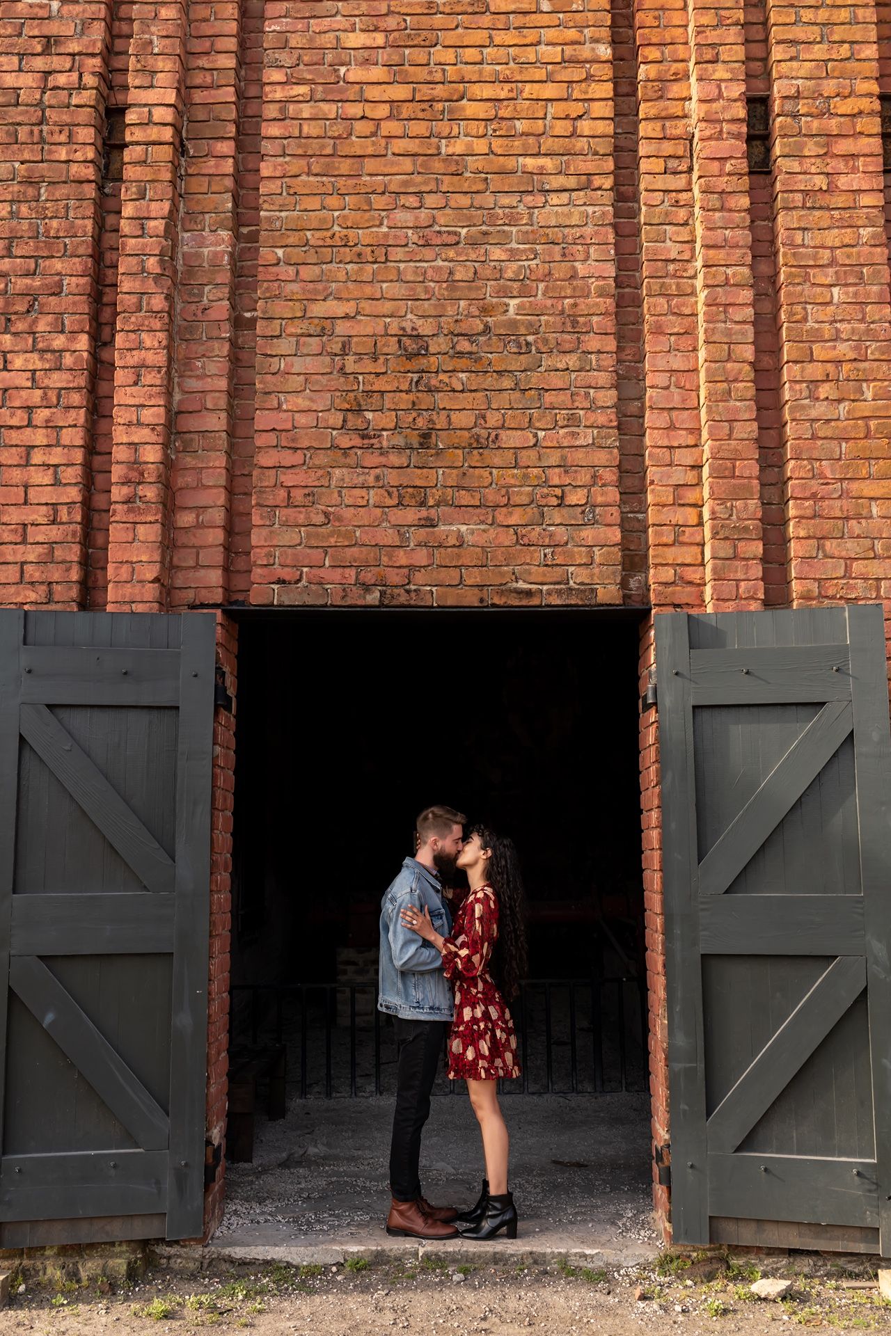 Romantic couple silhouetted in a rustic doorway with brick walls and dark gray doors at an industrial building.
