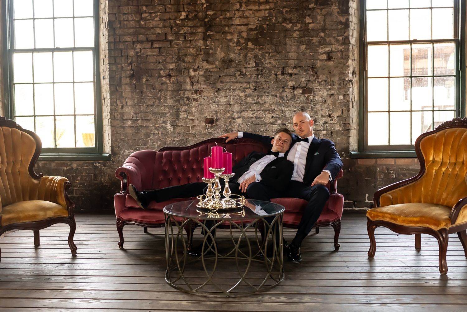 Two people lounge on an elegant chaise sofa in an industrial loft space with exposed brick walls and antique furniture.