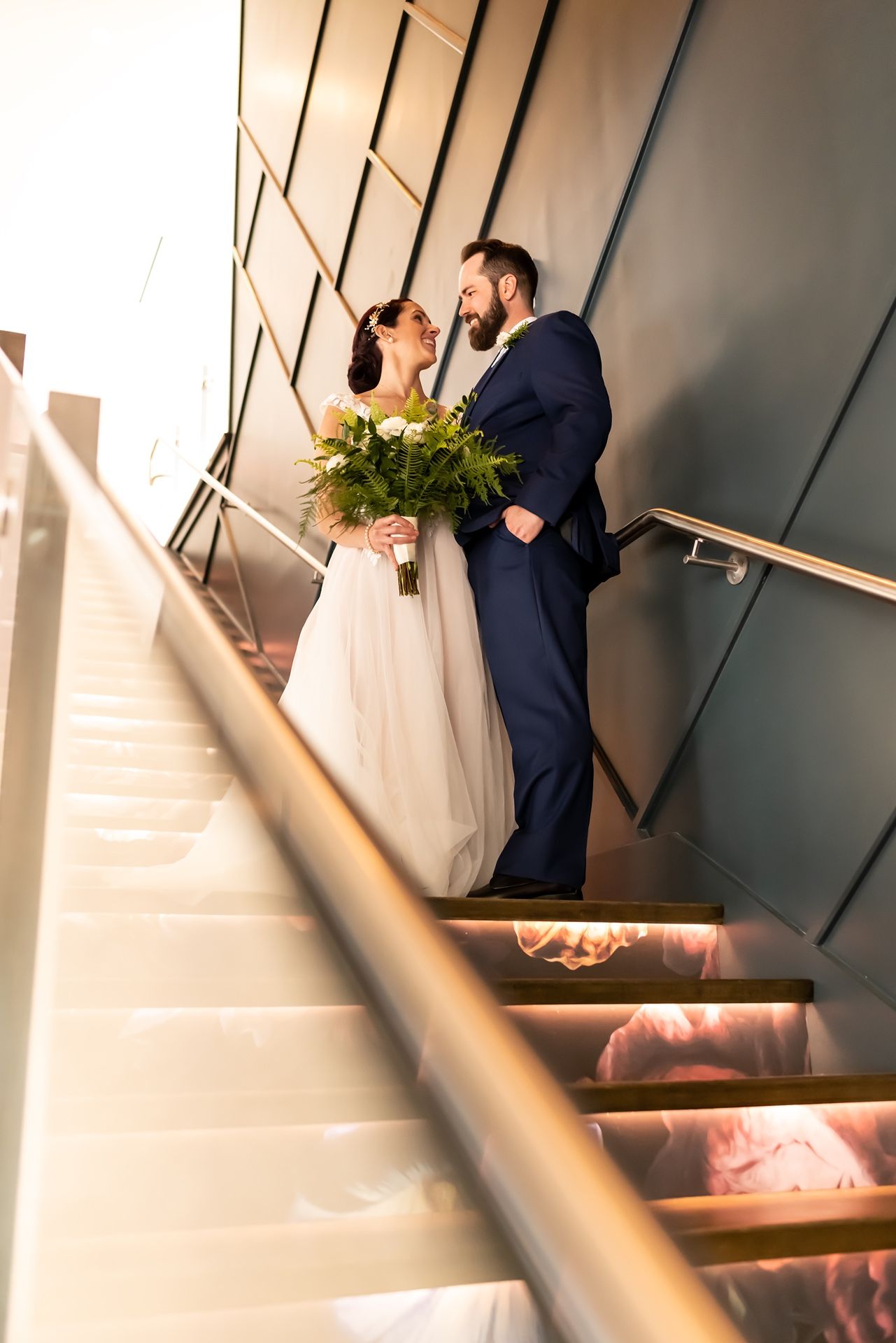 A couple share a romantic moment on a modern staircase with metallic railings and geometric wall details.
