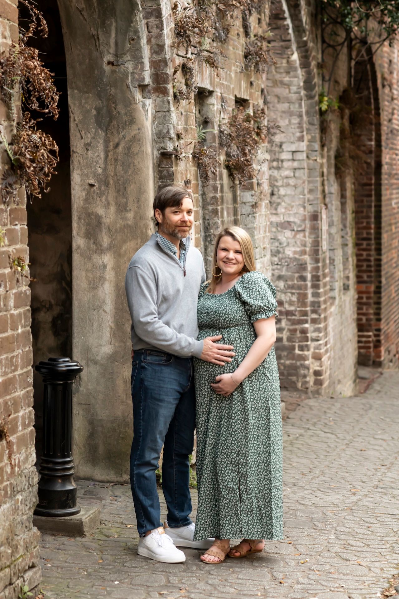 A couple embraces in front of rustic brick archways on a cobblestone street.