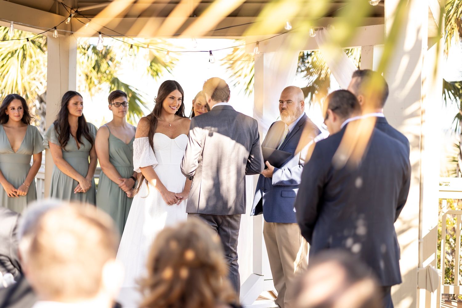 Wedding party guests converse and mingle on an outdoor patio decorated with beams and greenery.