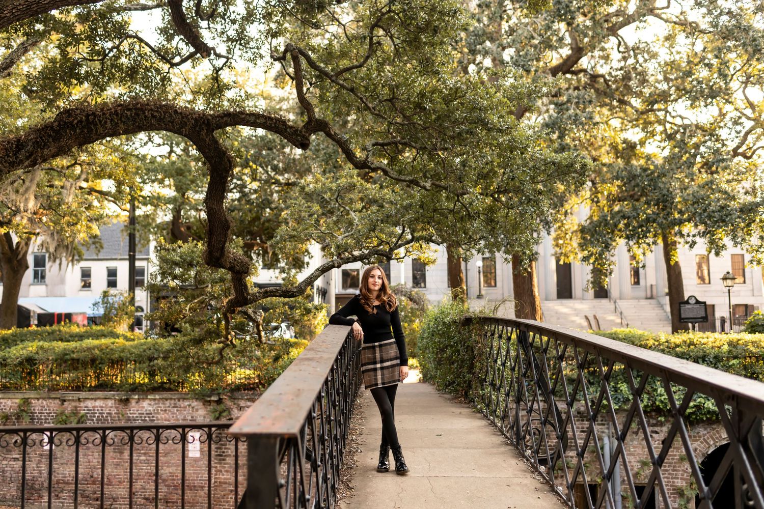A high school senior stands on a decorative bridge beneath moss-draped oak trees in historical Savannah, Georgia.