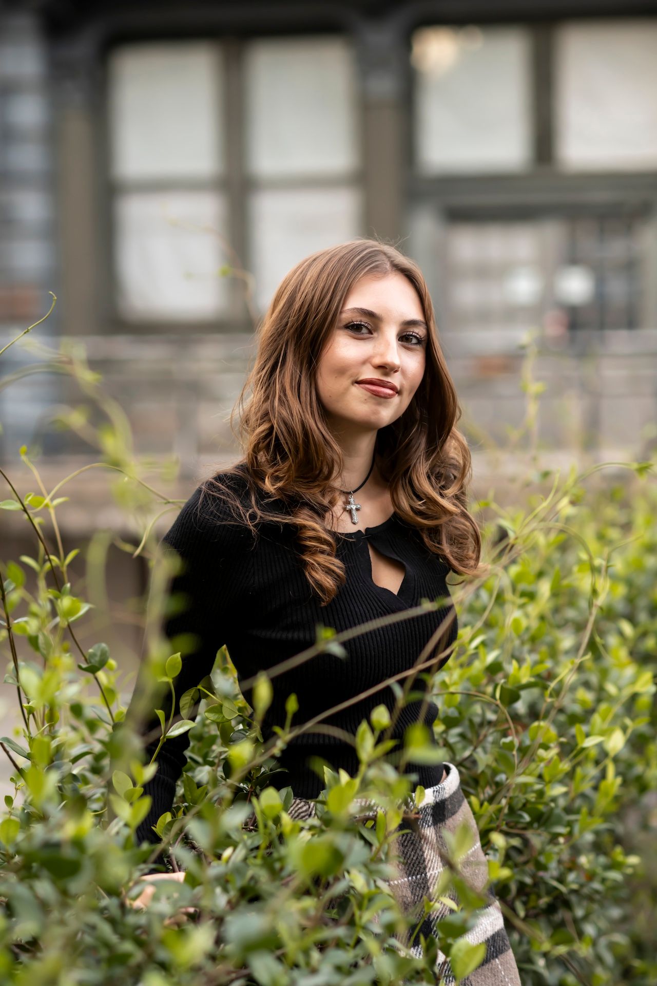 Someone wearing a black sweater poses thoughtfully among green foliage on an overcast day.