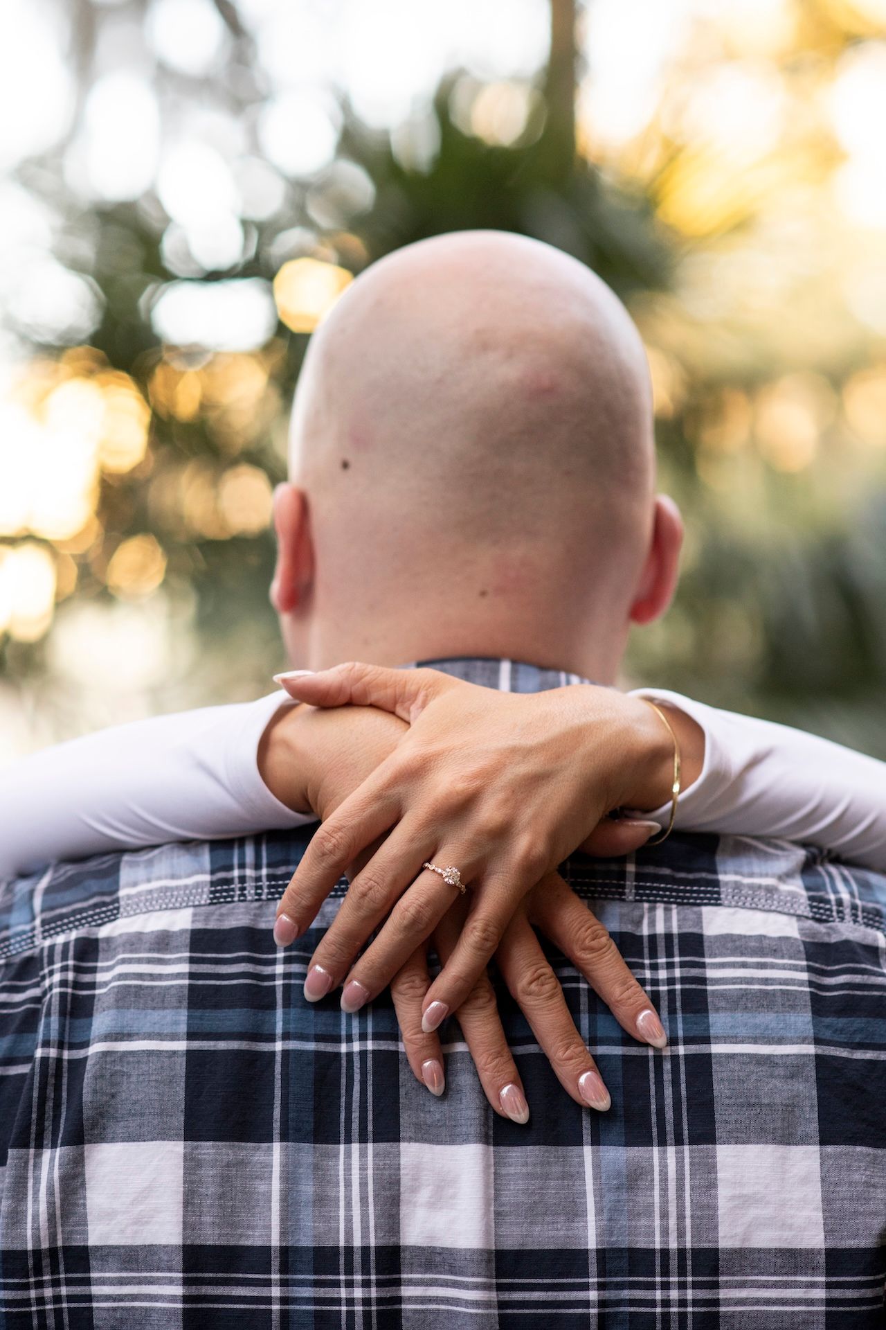 A rear view of a person wearing a plaid shirt with hands crossed on their shoulders in an intimate embrace.