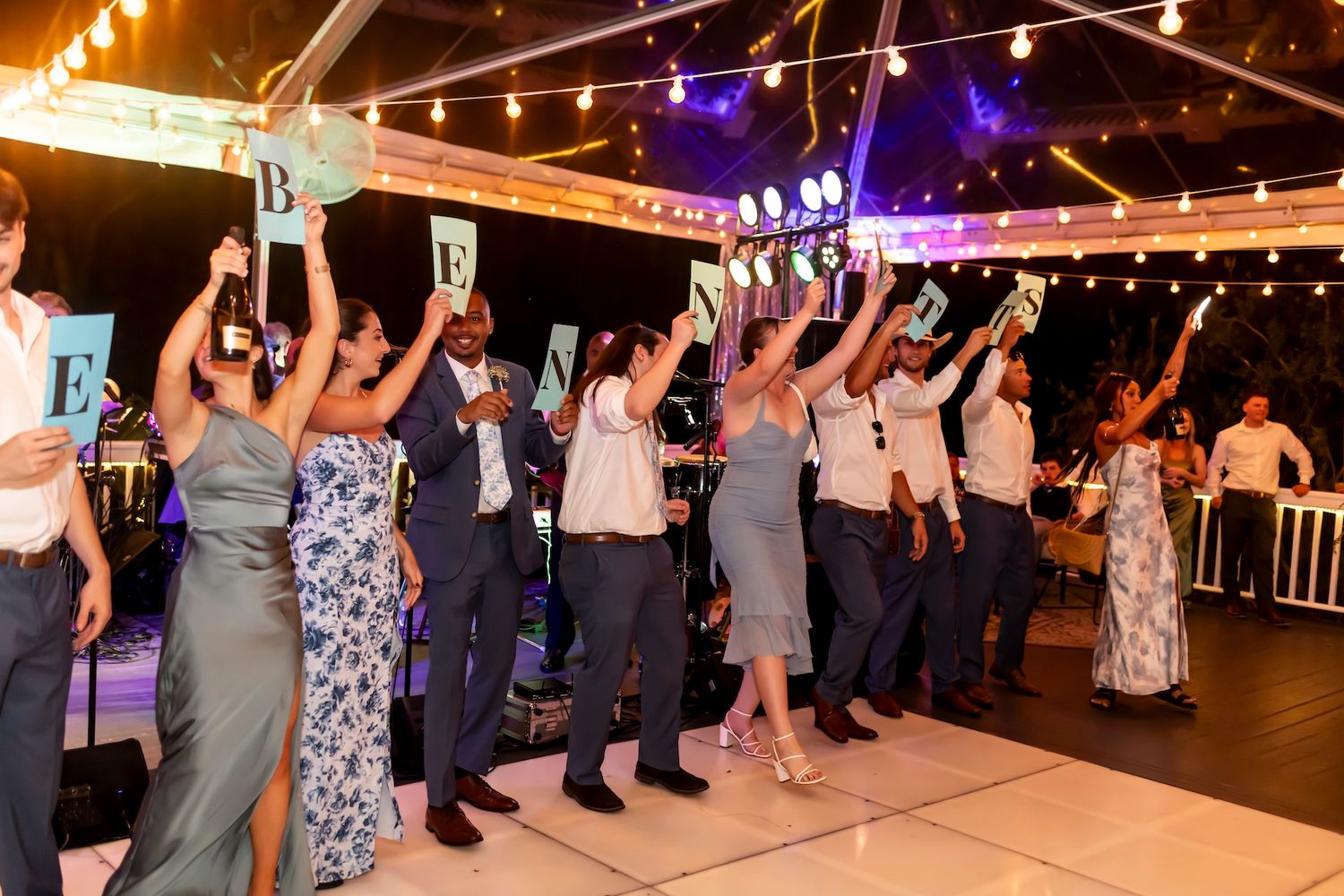 Wedding reception celebration with guests dancing under glowing string lights.