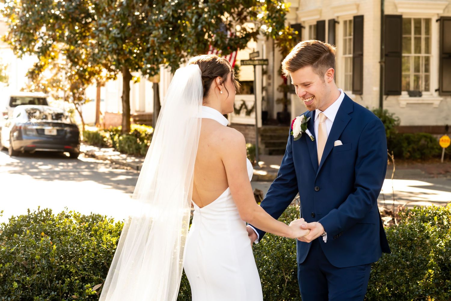 A couple smiles joyfully together on their wedding day, surrounded by lush greenery and golden sunlight.