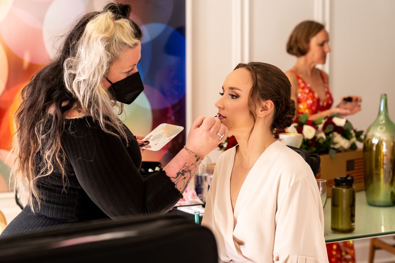 Makeup artist applying cosmetics on a person wearing a pink robe during a beauty preparation session.