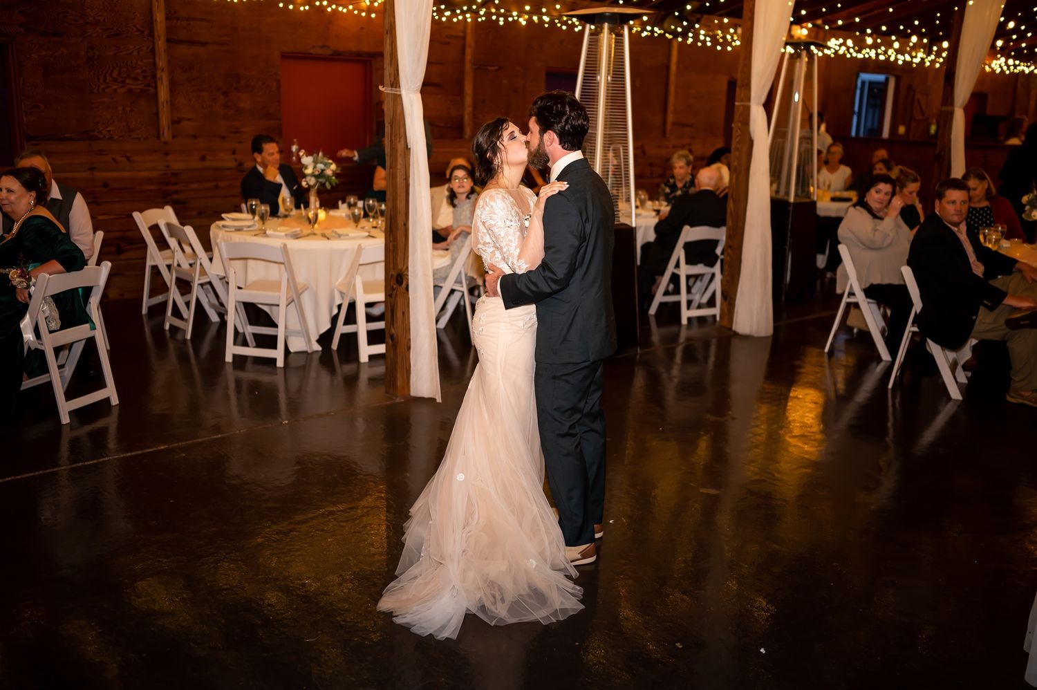 Dancing under warm string lights at an elegant wedding reception in a rustic venue.