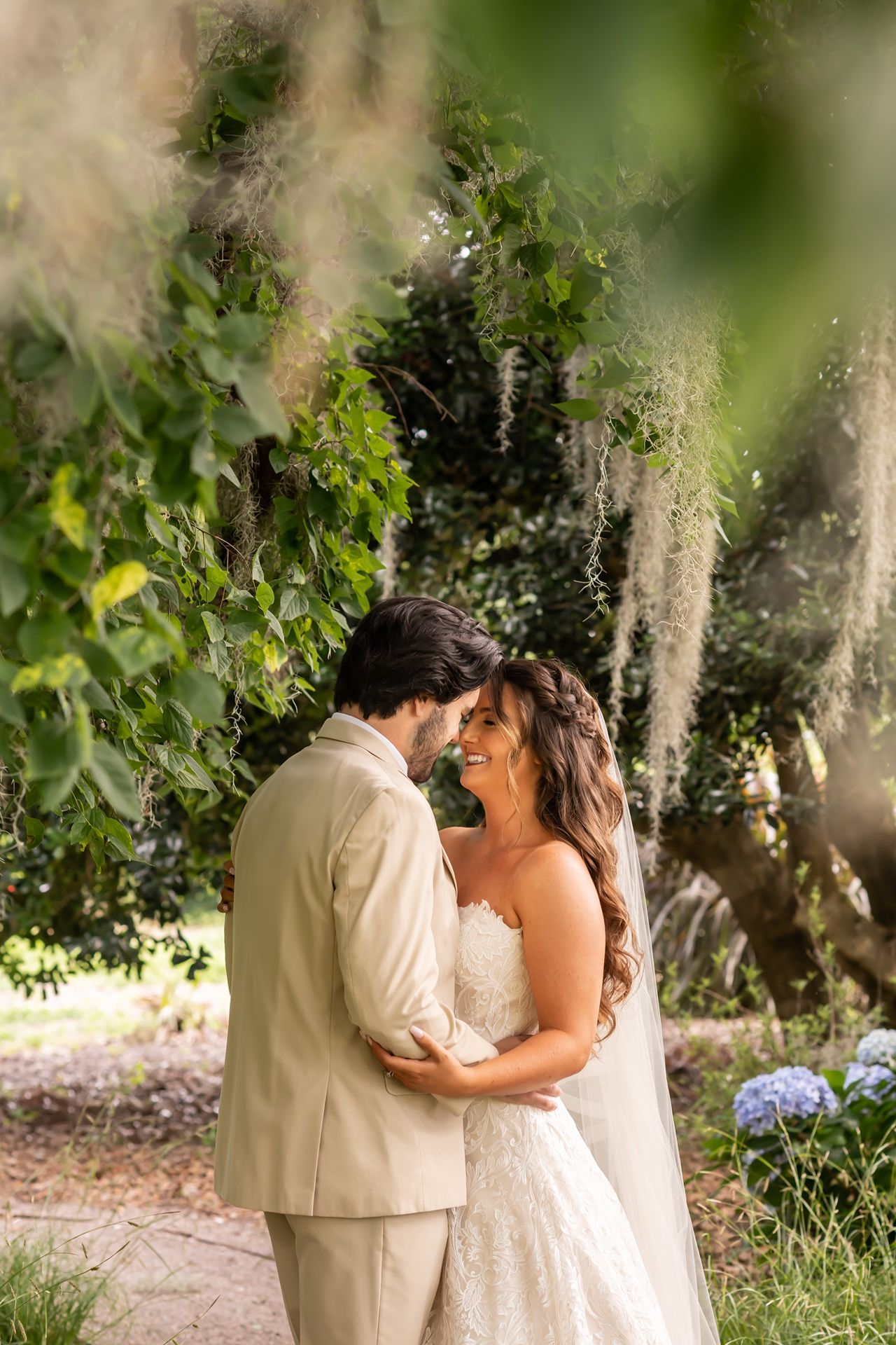 A romantic couple shares an intimate moment together in a sunlit garden setting with green foliage in the background.