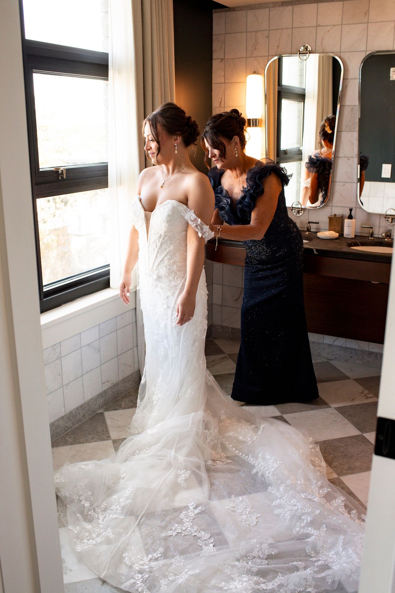 A wedding dress train trails elegantly across a tiled floor as final preparations are made in a bridal suite.