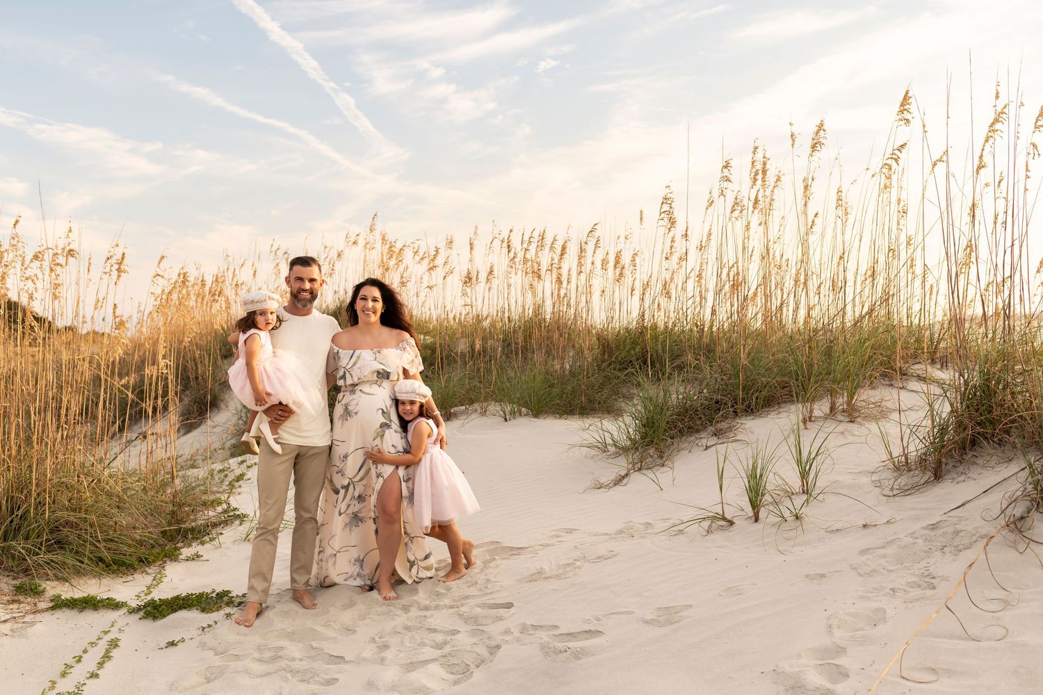 Family poses together on beach path through sea oats at sunset.