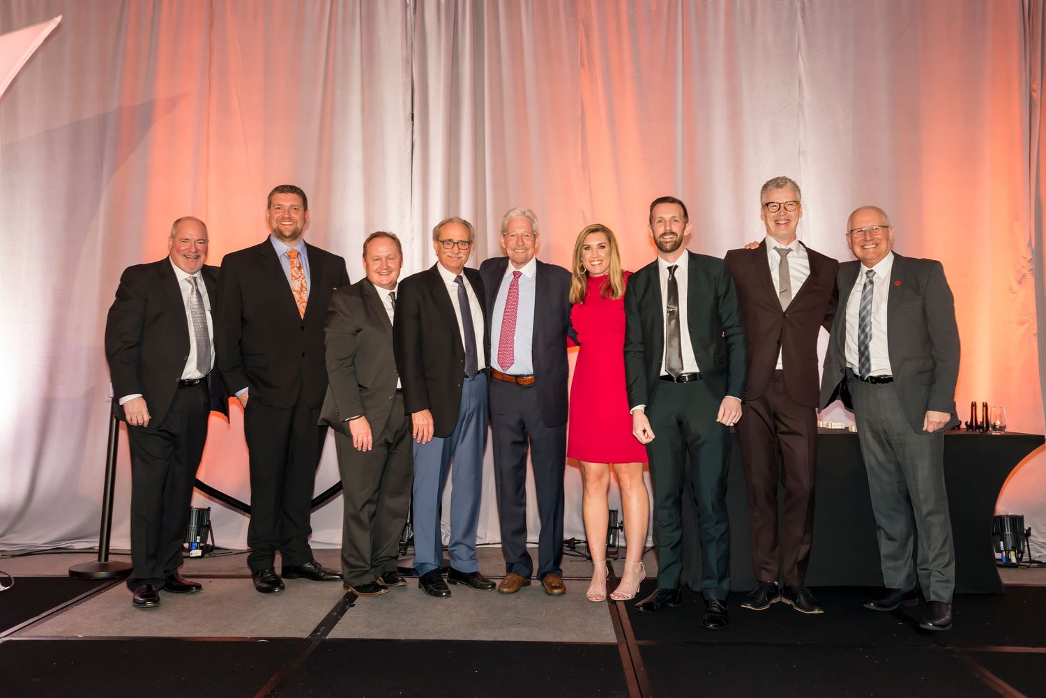 Group photo of business professionals posing together at formal event with decorative backdrop.