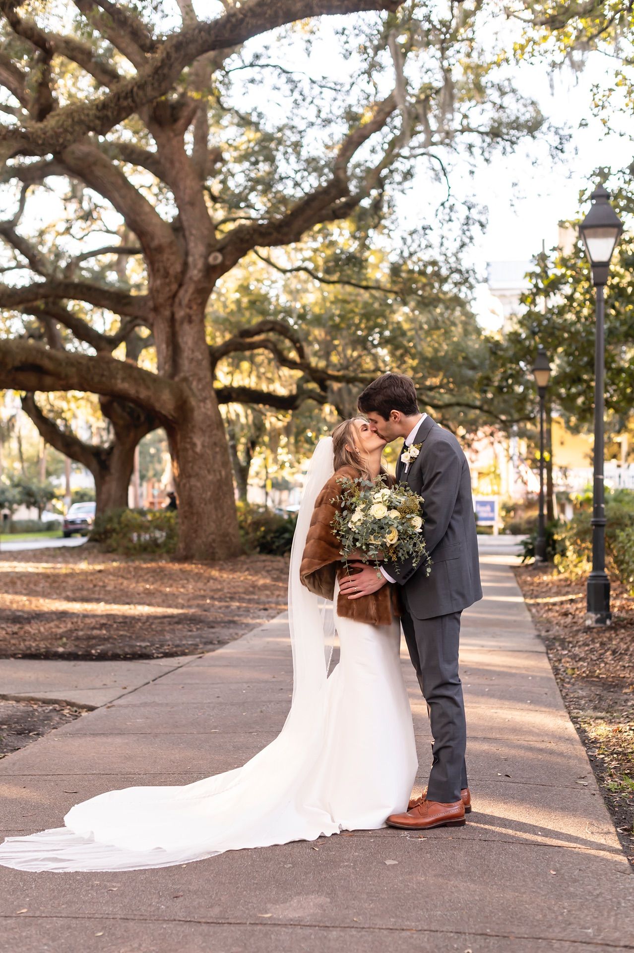 A romantic wedding couple shares tender moments under majestic oak trees during golden hour.