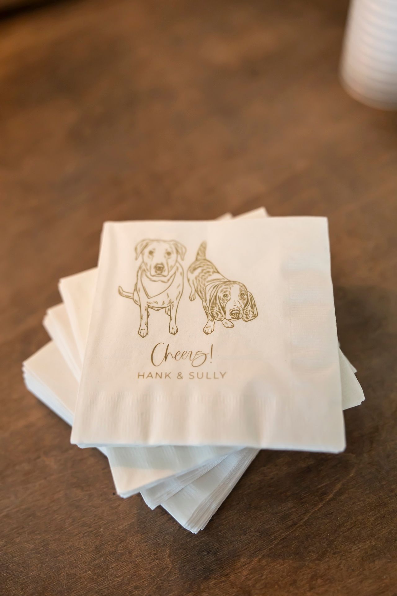 Custom printed white cocktail napkins with elegant gold text and logo designs displayed in a sequence.