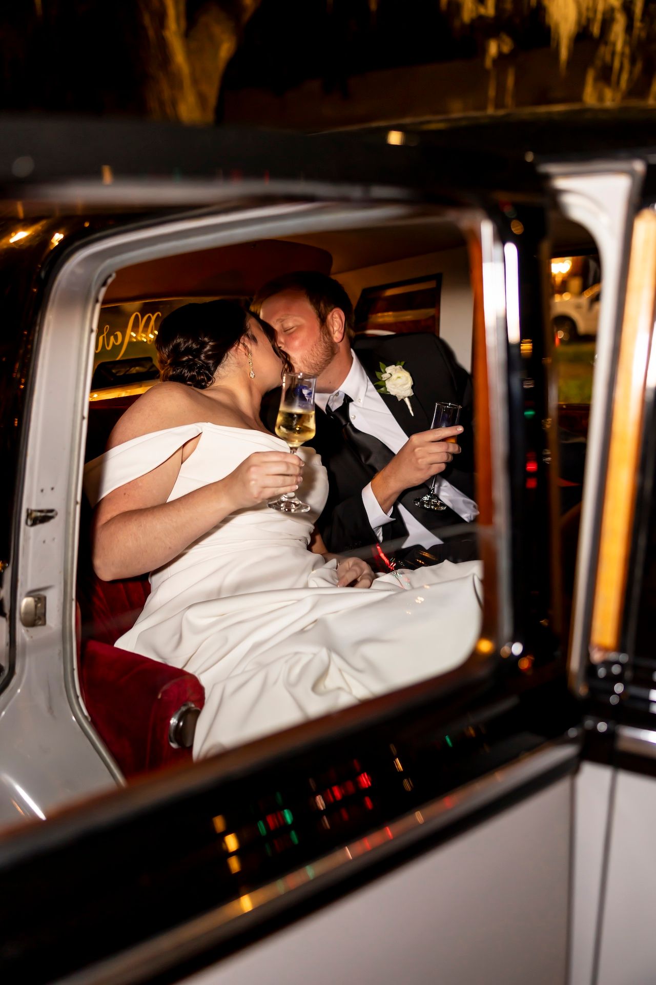 Newlyweds share an intimate moment together in the back of a vintage car after their wedding celebration.