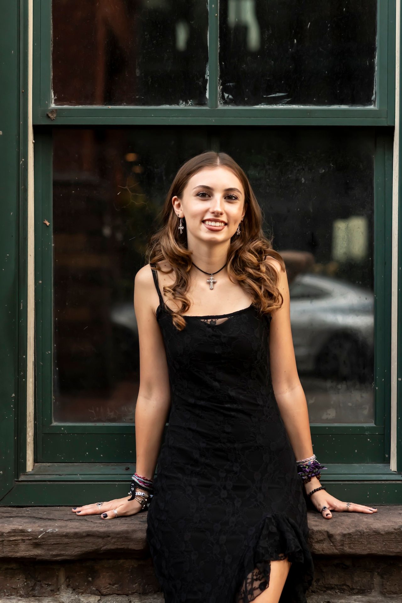 A person in a black velvet dress leans against a green window frame outdoors.