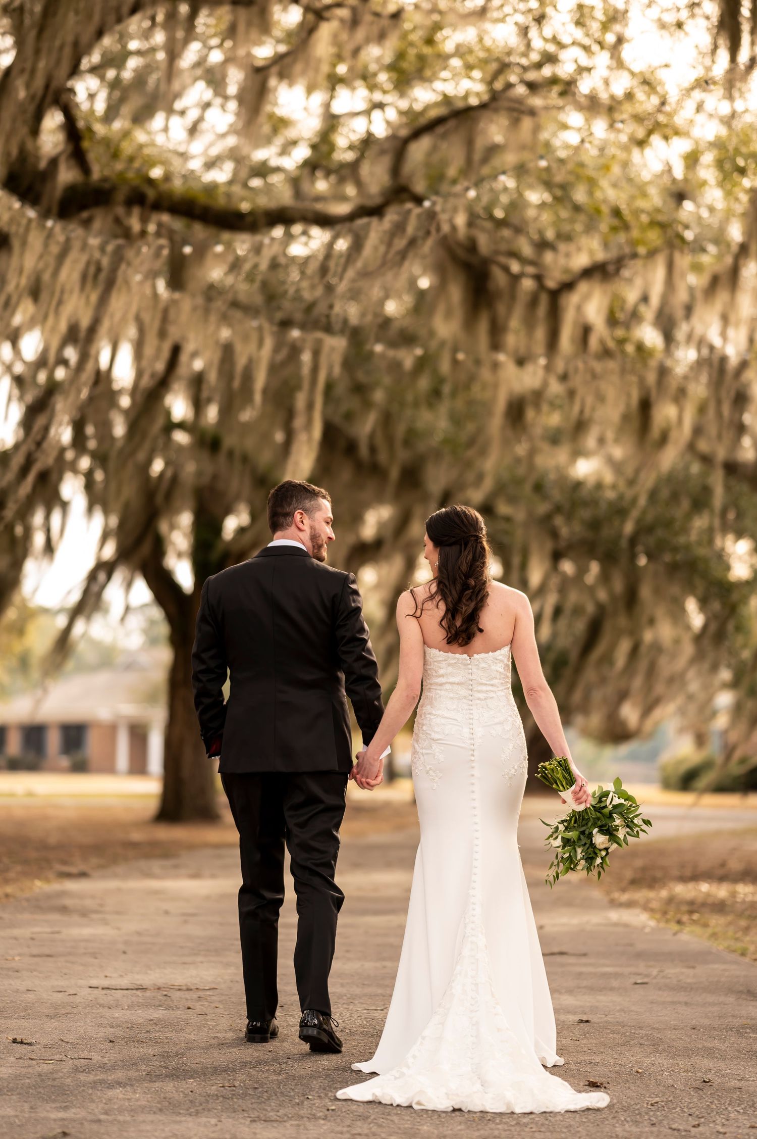 A romantic moment between newlyweds walking under moss-draped oak trees at sunset in the American South.