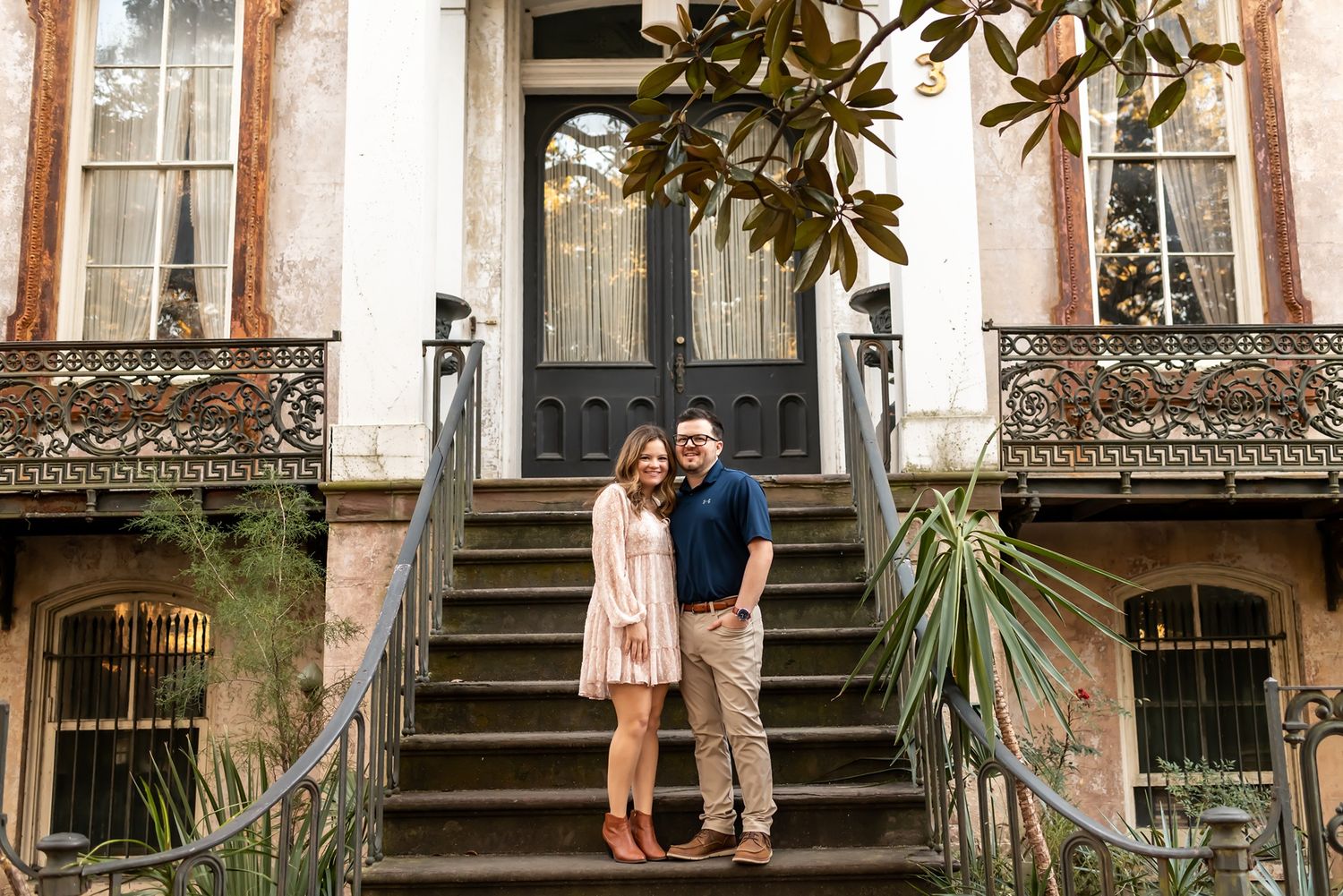 Happy couple standing on steps of historic building with ornate ironwork in Savannah.