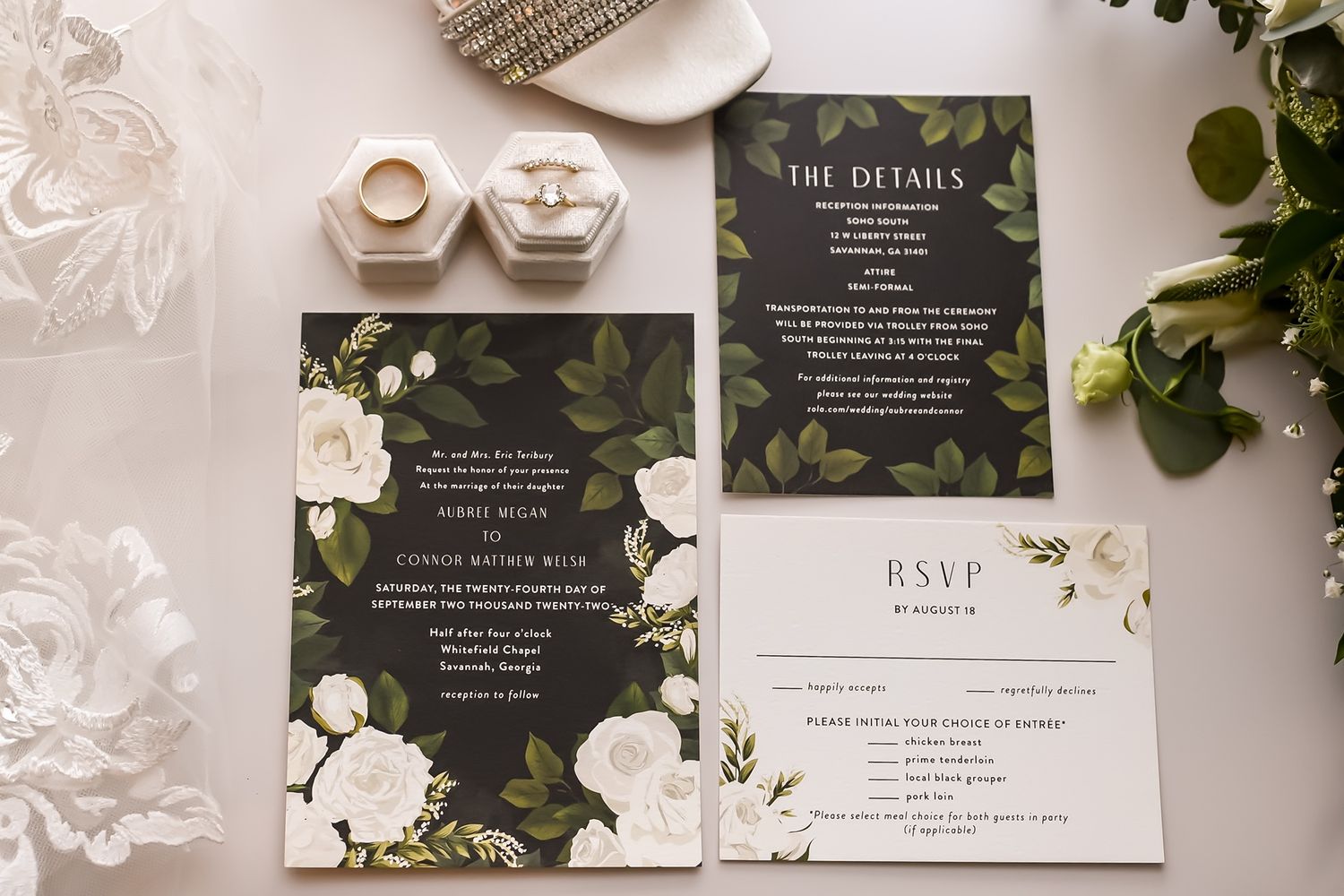 Wedding invitation suite featuring dark moody floral designs, white roses, and elegant typography on a marble background.