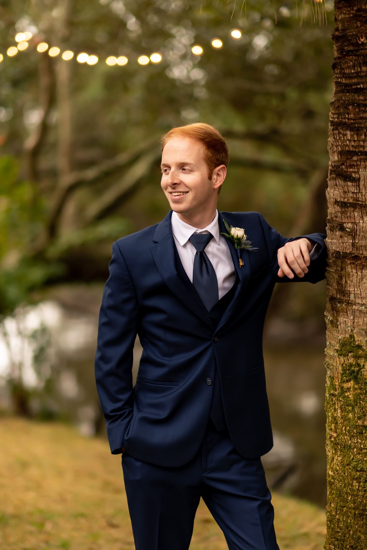 Wedding portrait sequence showing groom in navy suit posing between trees in outdoor natural setting.