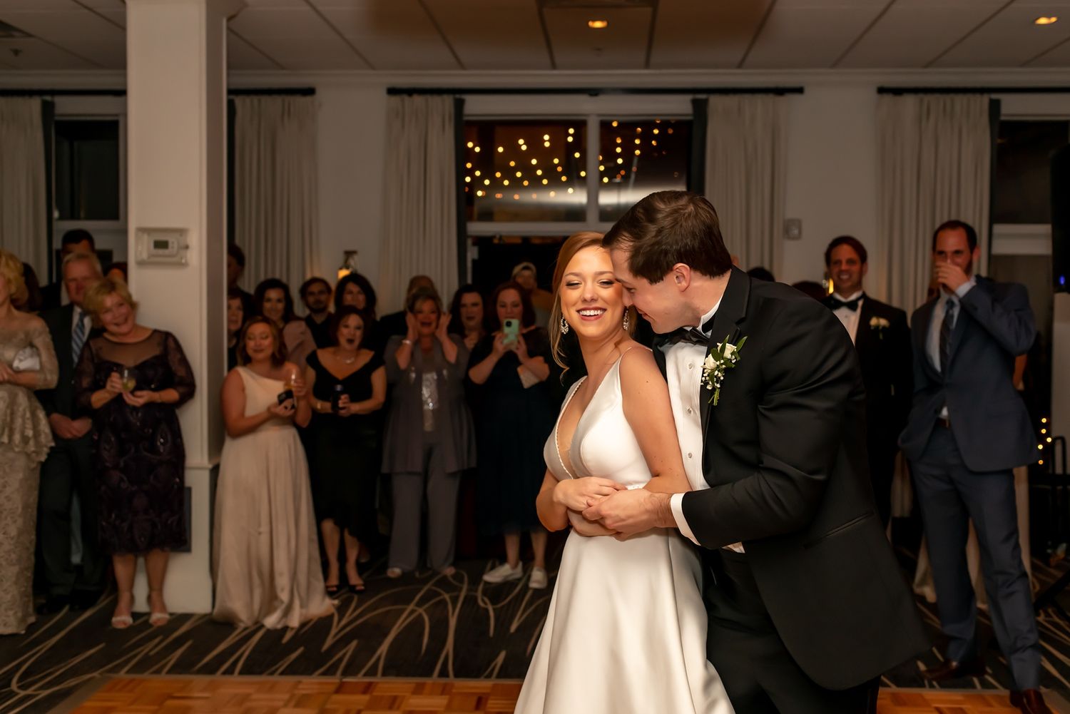 A couple shares a romantic first dance at their wedding reception while guests watch and smile from the background.
