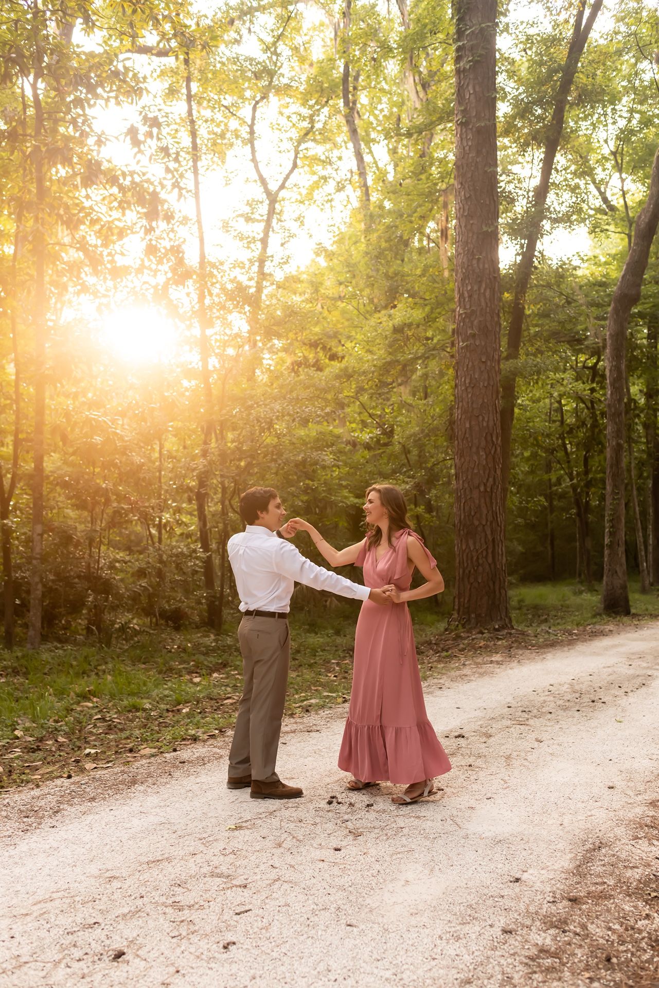 A couple shares a romantic dance together on a sunlit forest path during golden hour.