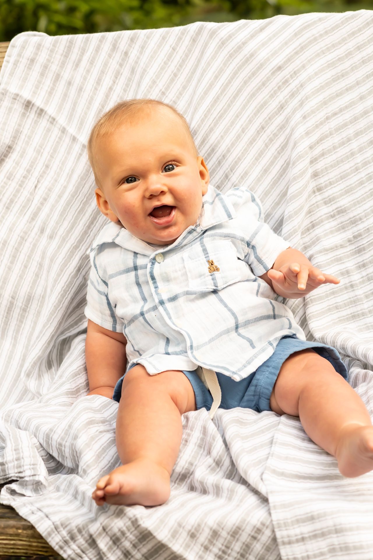Happy baby lying on striped bedding wearing a light blue outfit and showing joyful expressions.